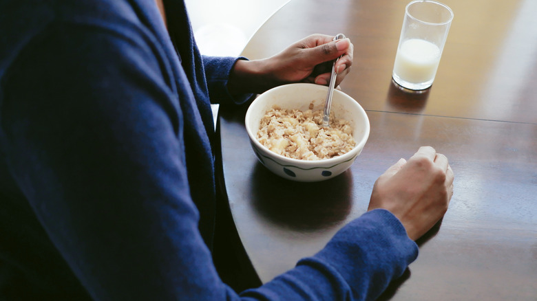 Black woman wearing a dark blue cardigan eating a bowl of oatmeal with a glass of milk on the table