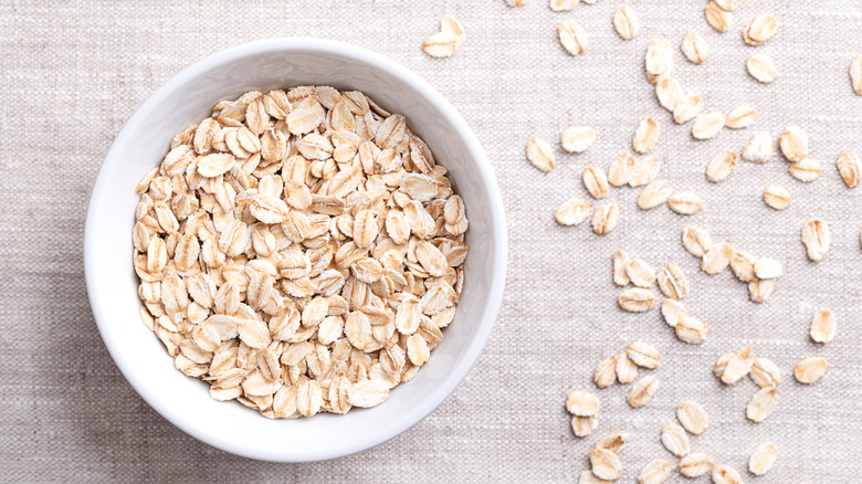 bowl of oats on neutral tablecloth with oats scattered next to it