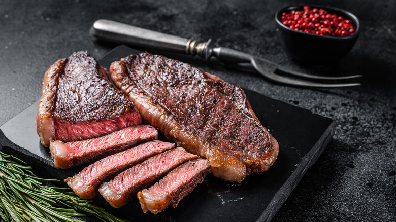 Grilled tenderloin on a black cutting board, with herbs to the side and a fork and bowl of berries in the background