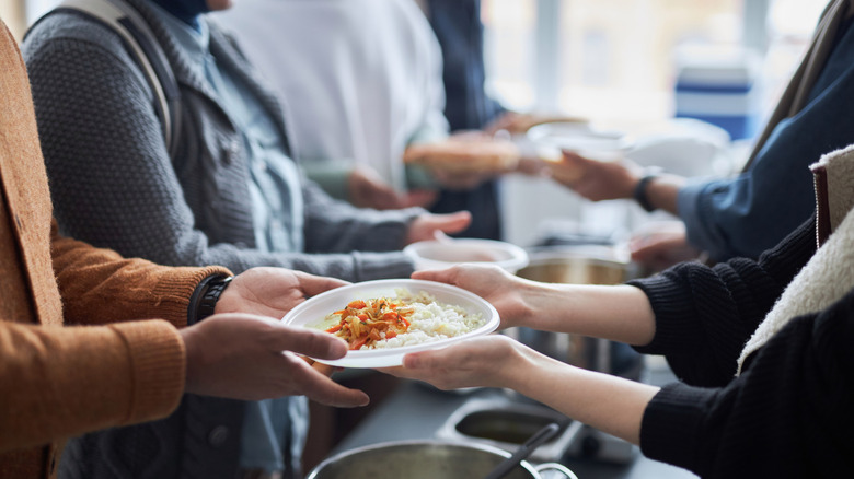 Volunteers passing food to people at a soup kitchen-type setup.