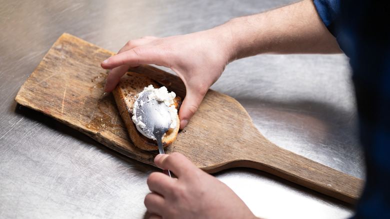 Person spreading cream cheese onto slice of toasted bread.