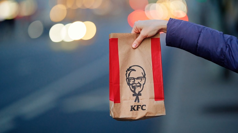 a hand extends with a bag of kfc takeout