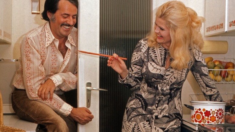a woman teases a smiling man in a 1970s kitchen