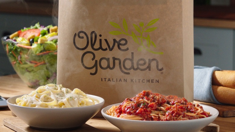 Olive Garden logo on paper bag, food in foreground.