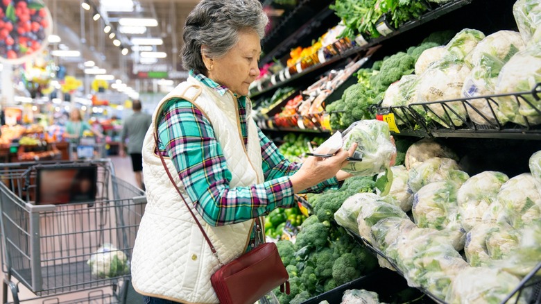 woman examines a head of lettuce at store