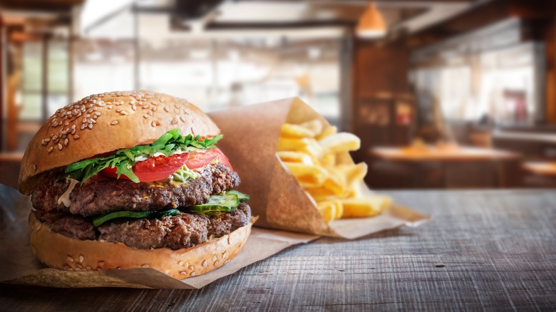 Fast food burger with fries on counter, generic fast food restaurant in background.
