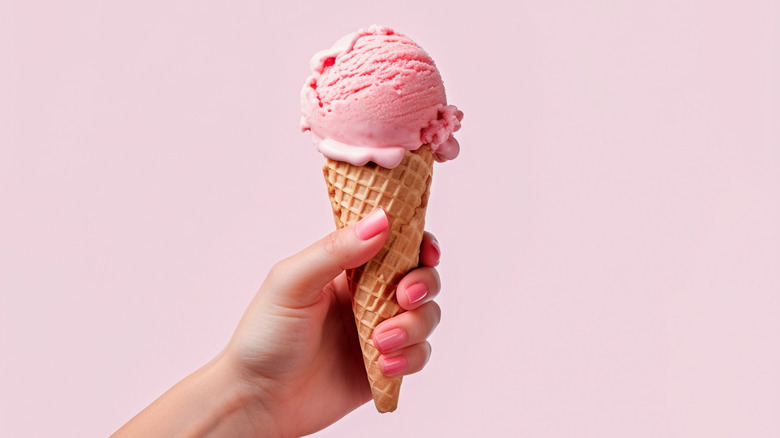 Hand hold strawberry ice cream in cone against pink background