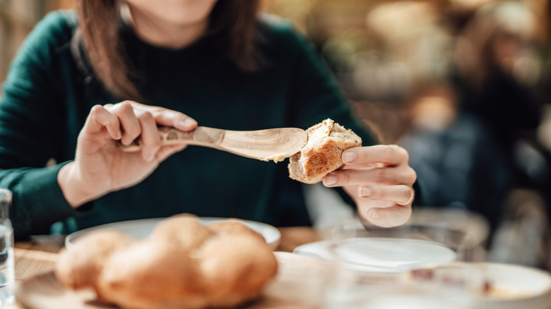 A woman butters a piece of bread at a restaurant