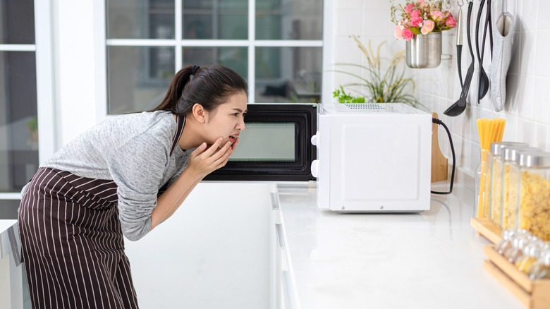 woman stares in confusion into her microwave