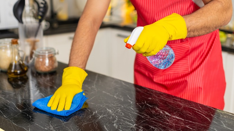 cleaning kitchen counter with gloves and spray