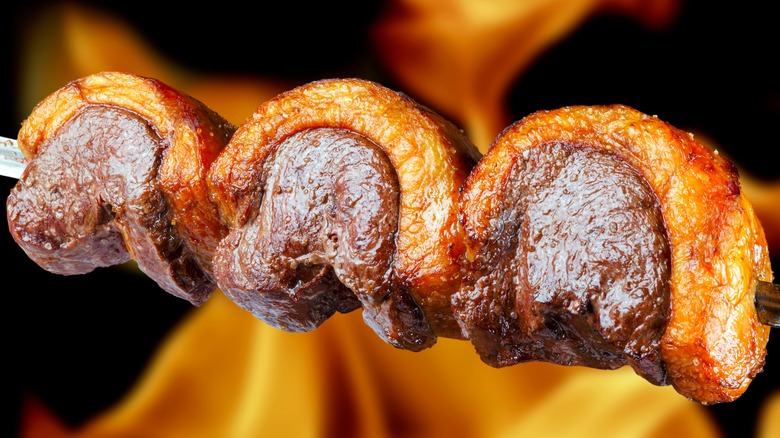 Roasted picanha on a skewer with flames in background