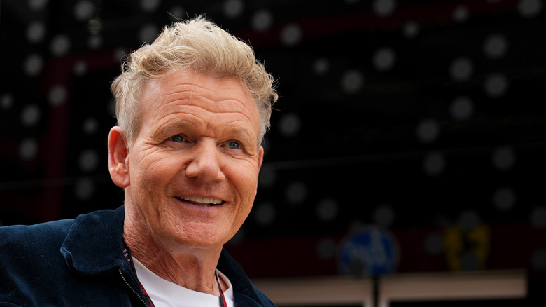 Gordon Ramsay smiling against dark, out-of-focus background.