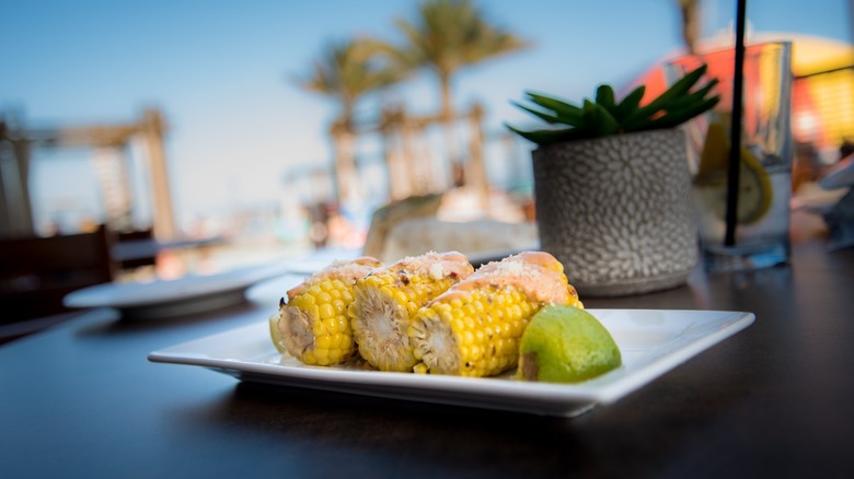 Grilled corn on the cob with chipotle butter, cheese, and lime on white plate.