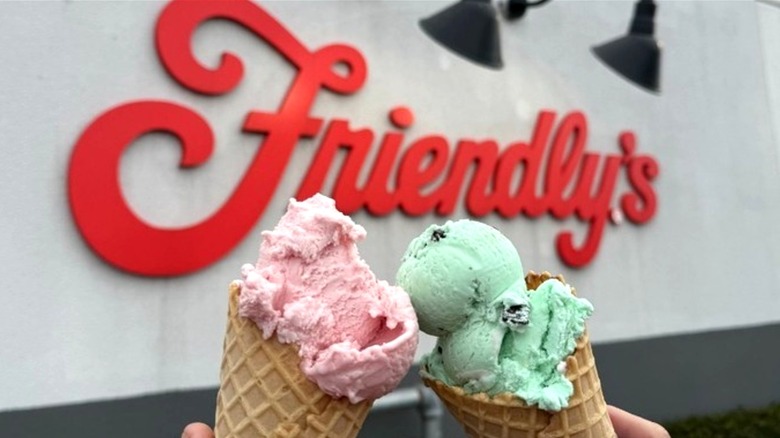 Hands holding two ice cream cones in front of Friendly's restaurant sign
