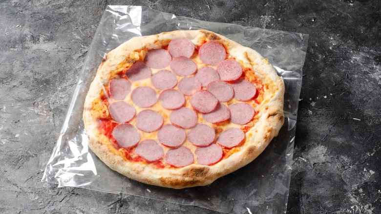 Frozen pizza in plastic wrapper on dark background