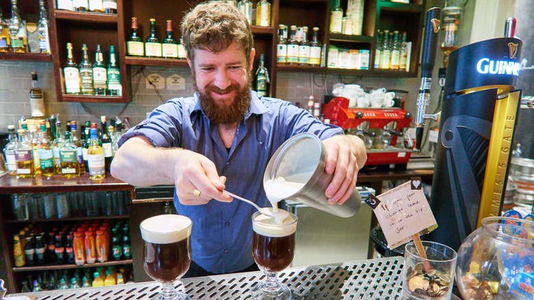Irish barkeeper spoons whipped cream into Irish Coffee