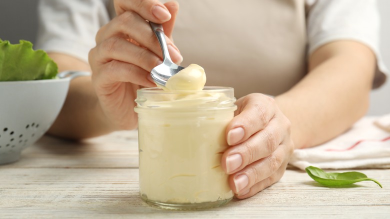 woman digging a spoon into a clear glass jar of mayonnaise