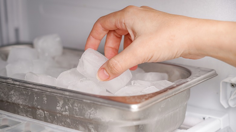 hand picking up an ice cube from metal tray