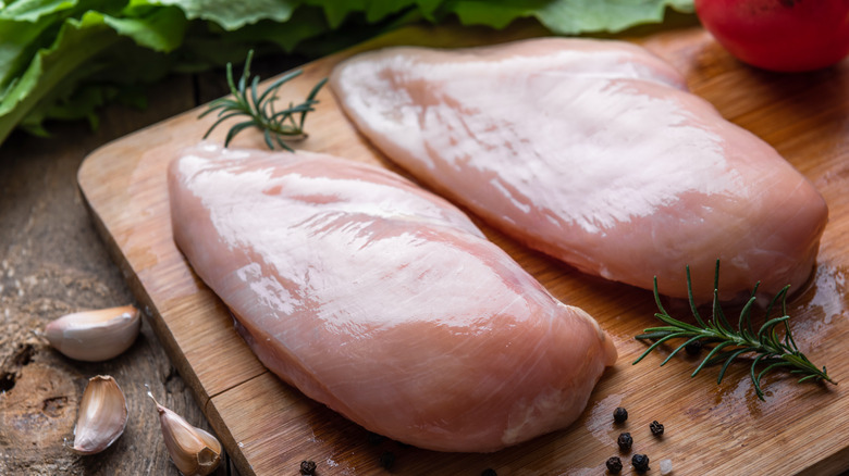 Two raw chicken breasts sit on a cutting board