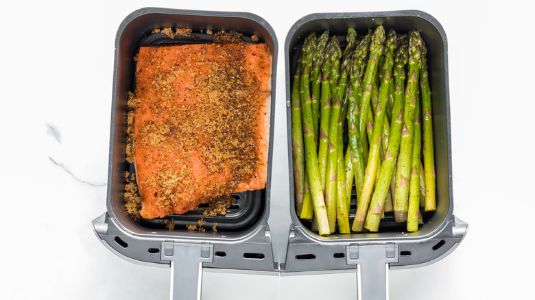 Two air fryer baskets, one with salmon and the other with asparagus