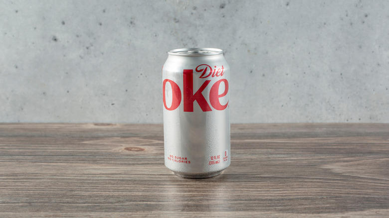 Can of Diet Coke on wood surface, gray background.