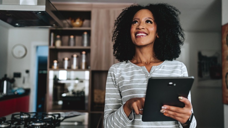woman on tablet looks around kitchen
