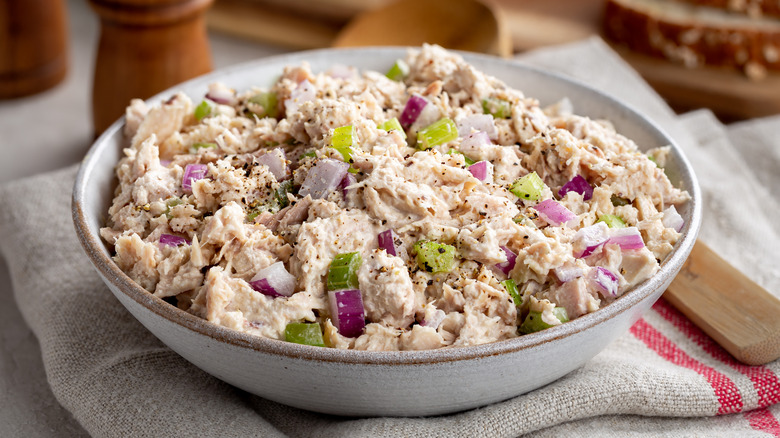 bowl of tuna salad with wooden spoon, pepper grinder and bread in background