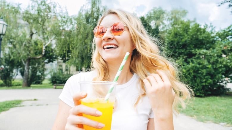 Woman with sunglasses holds cup of orange juice