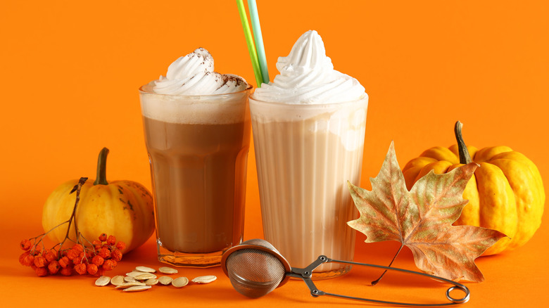 Glasses of hot pumpkin latte with whipped cream and seeds on orange background
