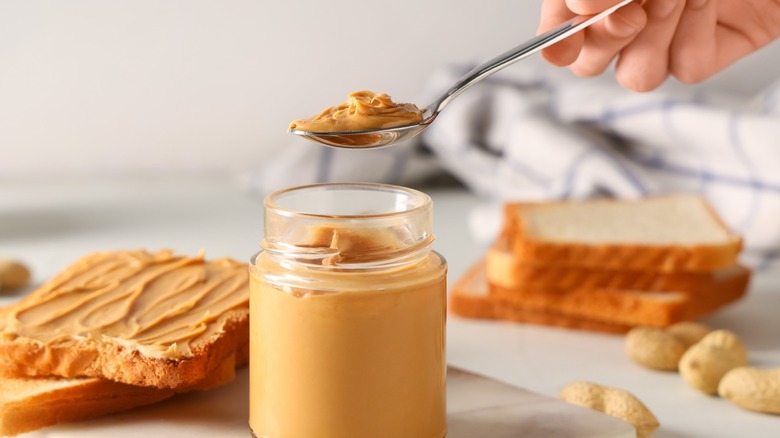a hand holds a spoon over a jar of peanut butter