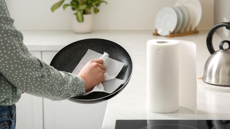 Someone cleaning a frying pan with a paper towel