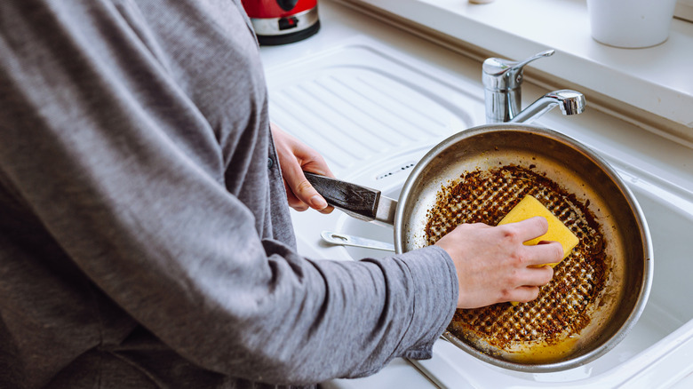 Someone scrubbing burnt residue off of a metal pan with a sponge