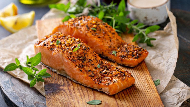 Grilled salmon on a wood plank with lemons and herbs in background