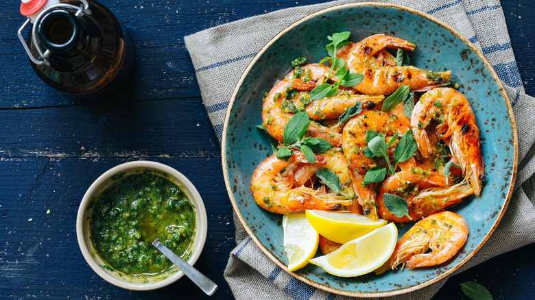 Grilled shrimp in a bowl with lemons and chimichurri on the side