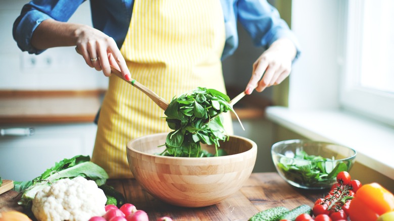 home cook in apron tosses dressed salad