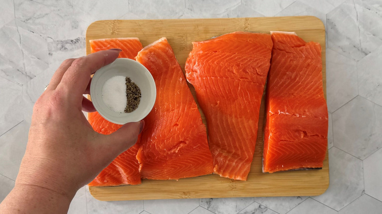 Hand holding small bowl of salt and pepper over salmon filets