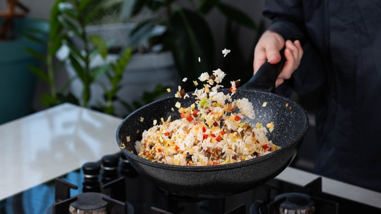 hand tosses rice in a skillet as it fries