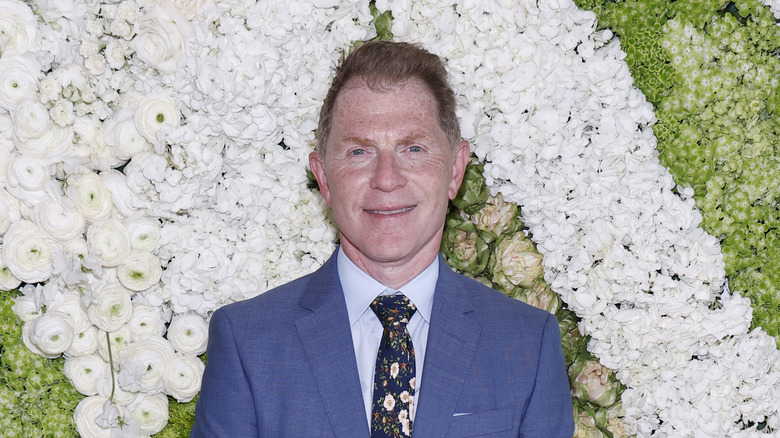 Bobby Flay smiling while standing against floral background.