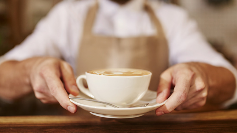 Waiter serving cup of coffee on a saucer with spoon.