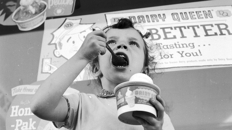 A young girl eating ice cream outside a Dairy Queen store