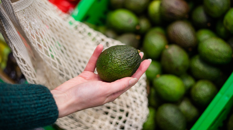 woman holding an avocado and a reusable grocery bag