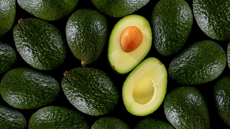 pile of whole avocados and one sliced avocado