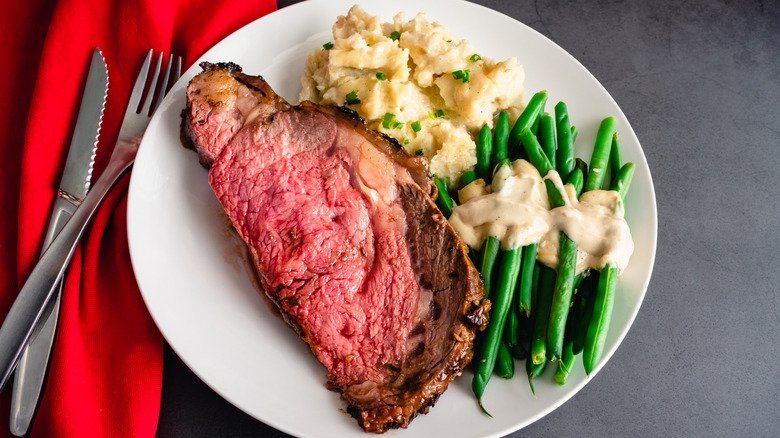 A cut of prime rib on a plate with mashed potatoes and asparagus