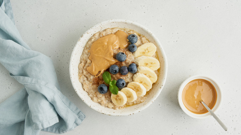 A bowl of oatmeal with blueberries, bananas, and peanut butter, with a smaller bowl of peanut butter to the right