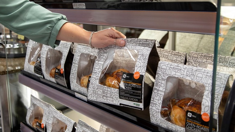 a hand grabs a publix rotisserie chicken from hot case