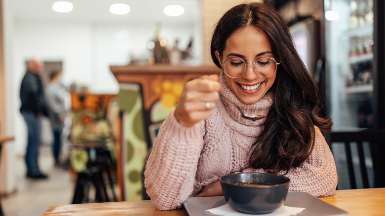 woman with glasses eats soup from bowl