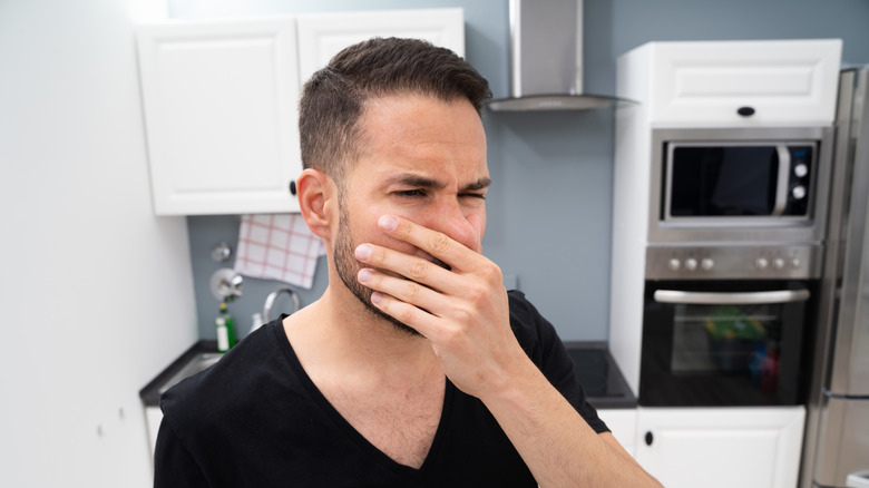 Man holding nose in bad smelling kitchen