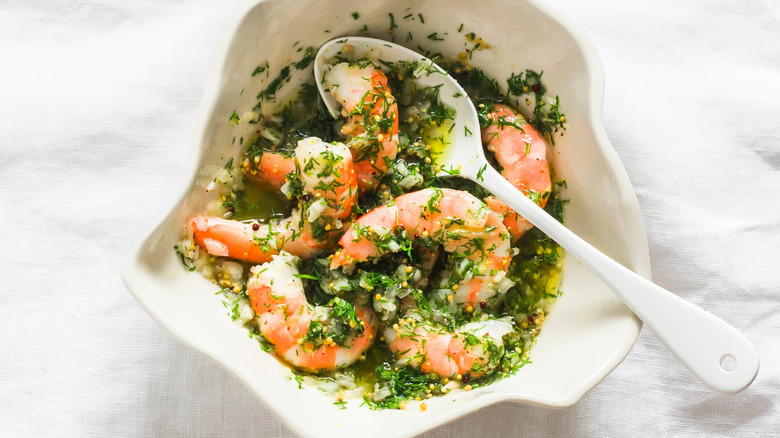 A bowl of shrimp in an herbaceous marinade with a spoon