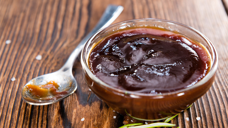 Close-up of small glass bowl of bbq sauce, with a spoon to the side.