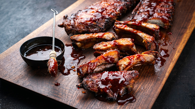 Close-up of BBQ ribs with small cup of BBQ sauce and brush to the side.